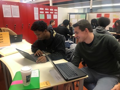 Two male students sitting at computers and smiling