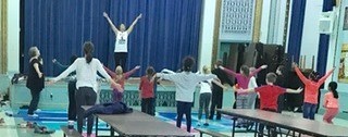 Elementary students on stage with arms stretched upward