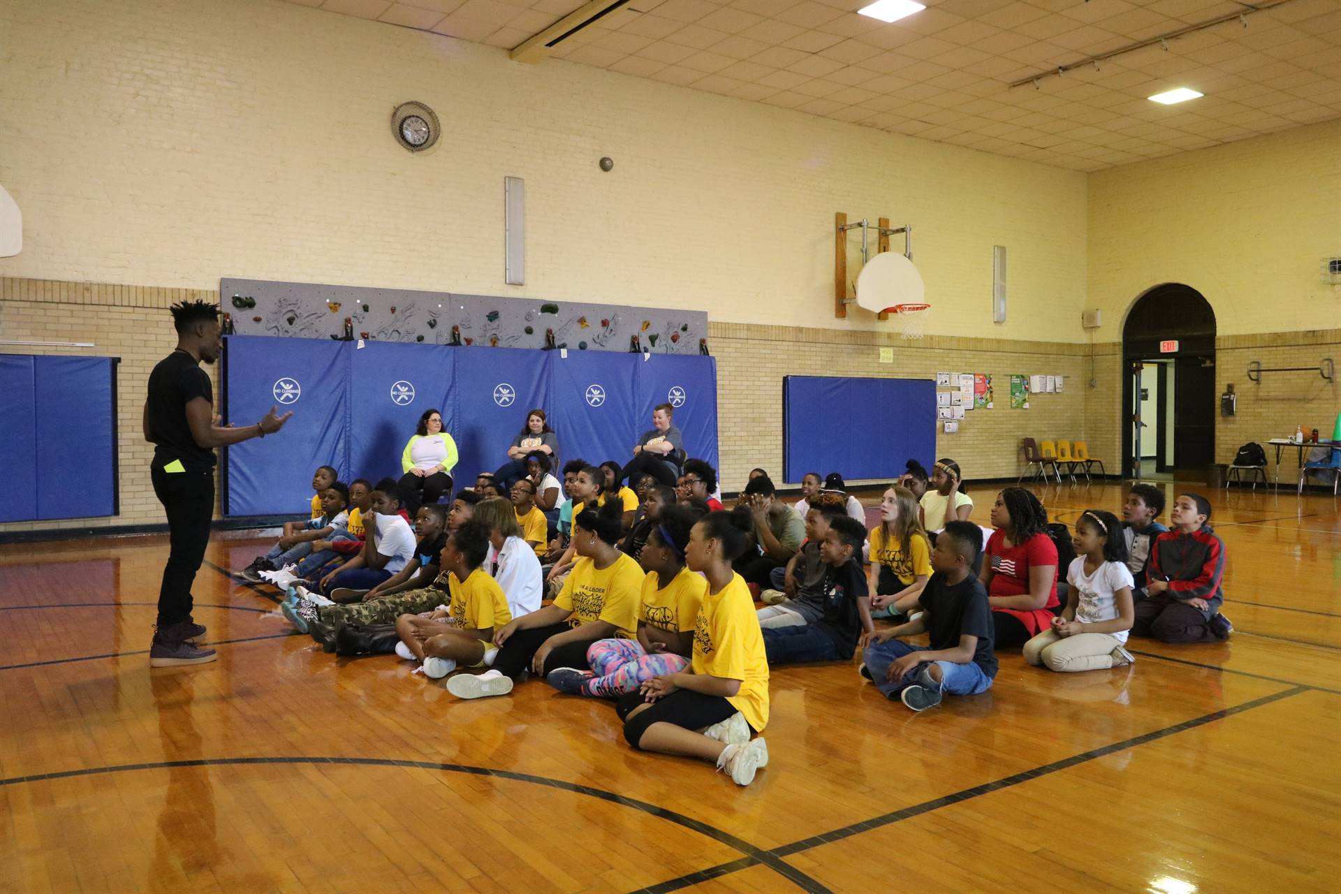 Motivational speaker talks to kids sitting on floor in Oxford gym