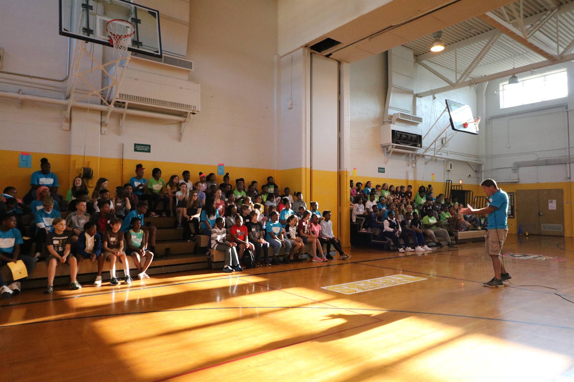 Students sitting in gym bleacher watching teacher speak