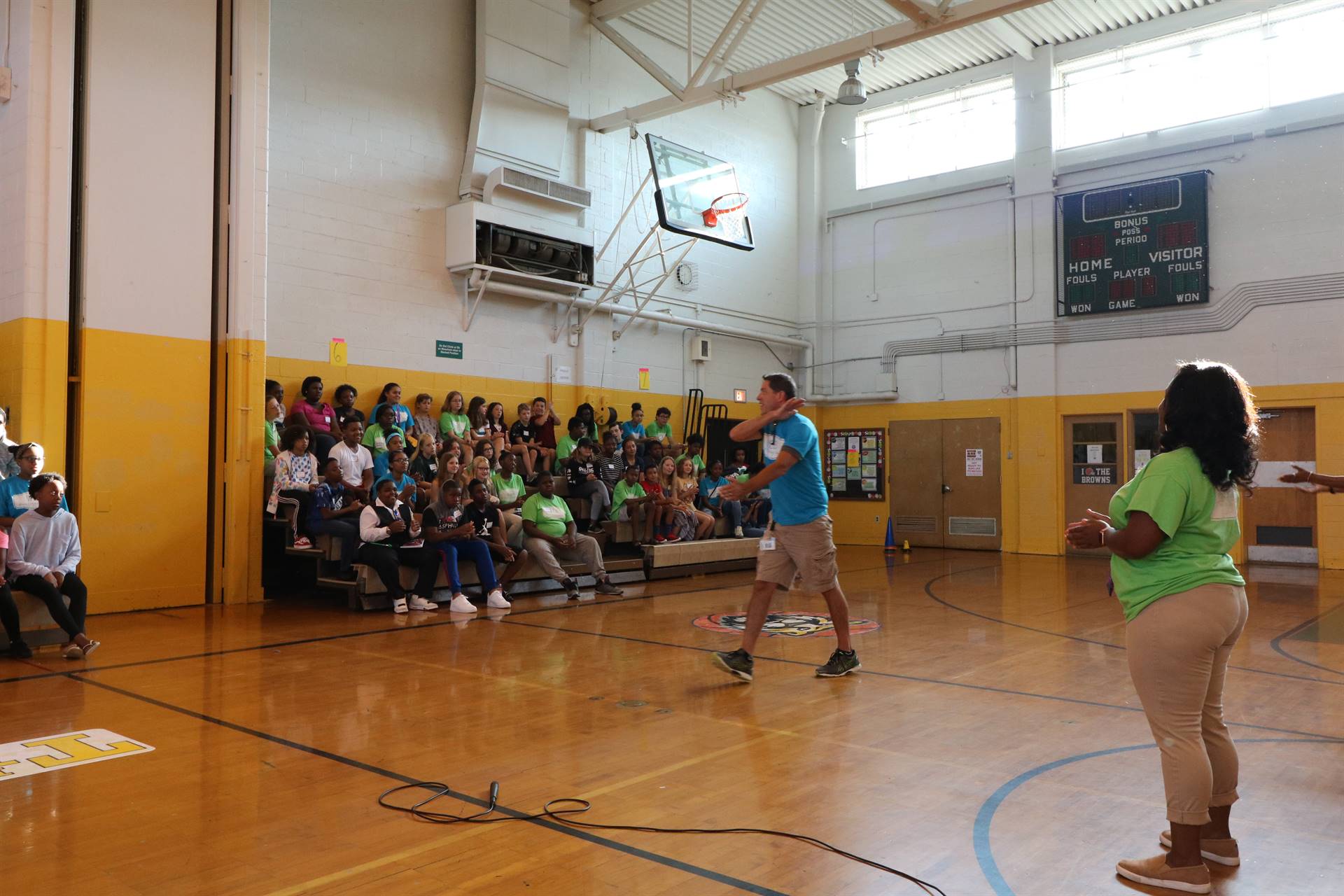 Students sitting in gym bleacher watching teacher speak