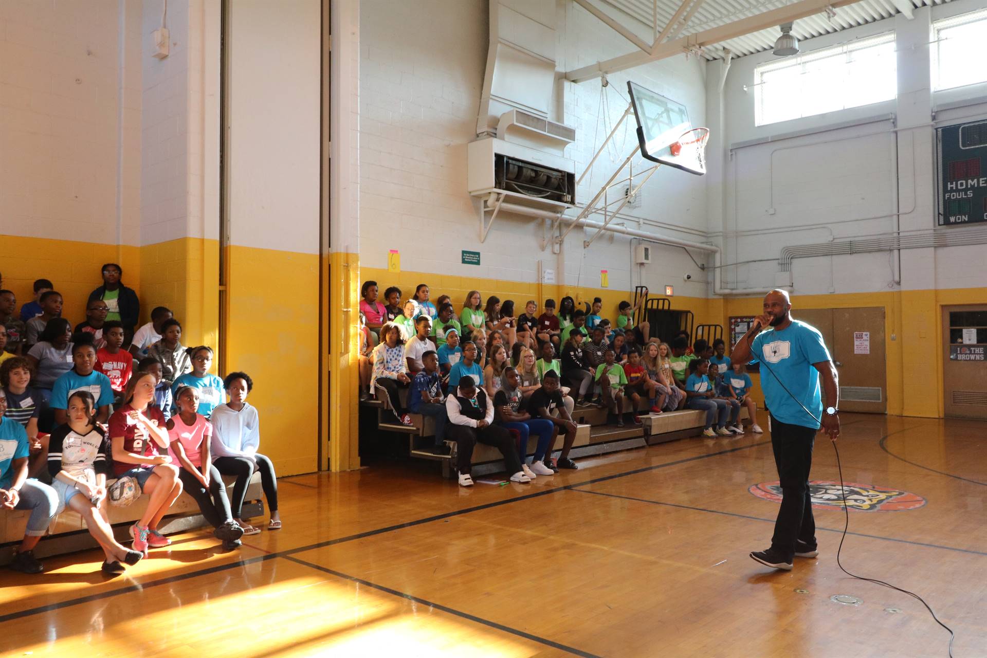 Students sitting in gym bleacher watching teacher speak