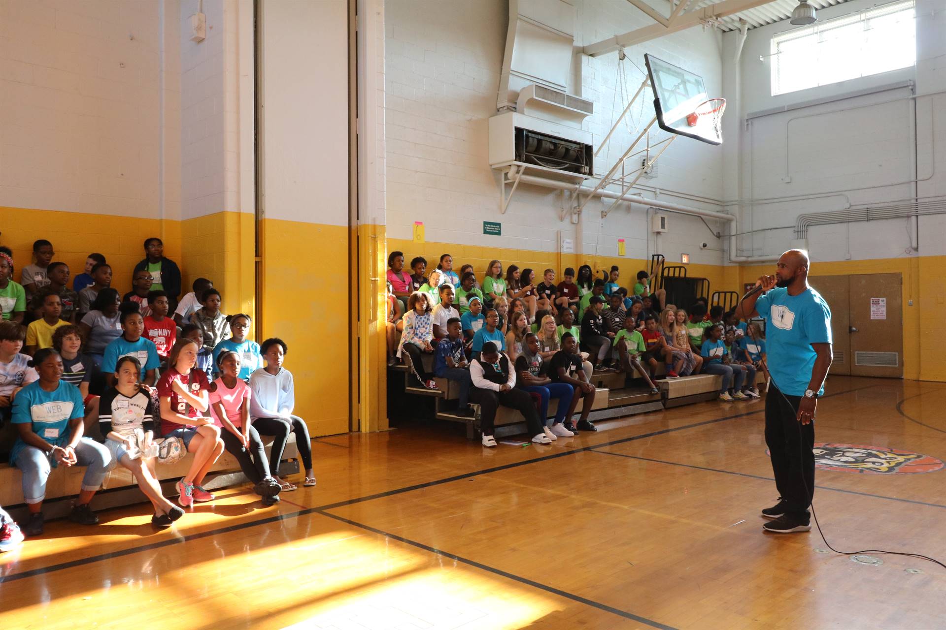 Students sitting in gym bleacher watching teacher speak