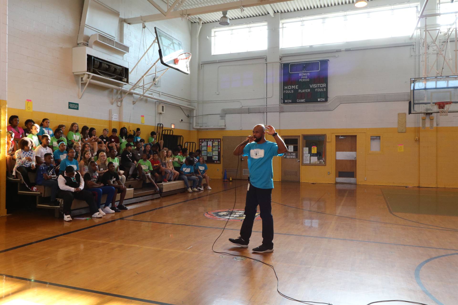 Students sitting in gym bleacher watching teacher speak