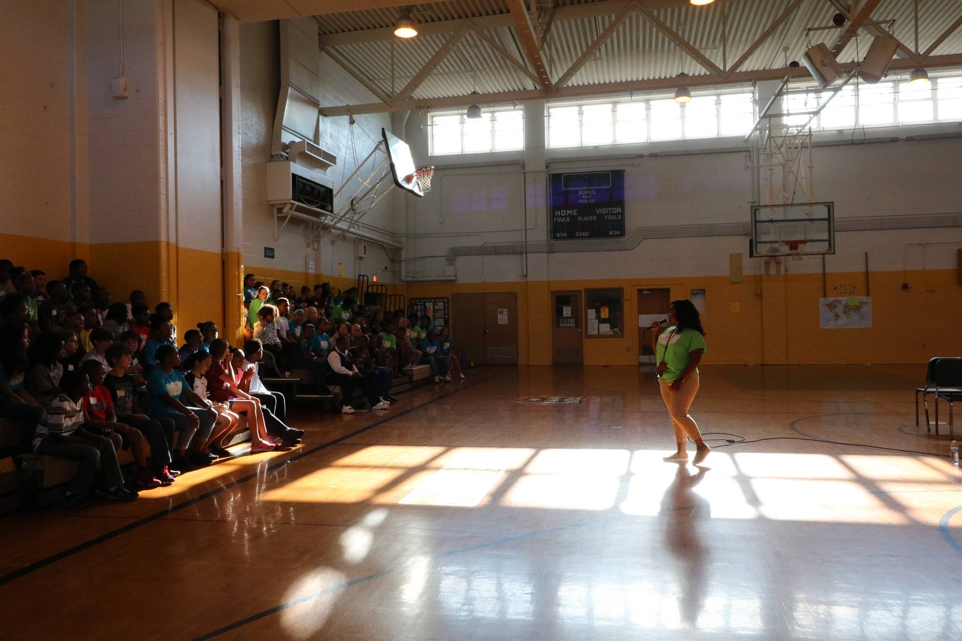 Students sitting in gym bleacher watching teacher speak