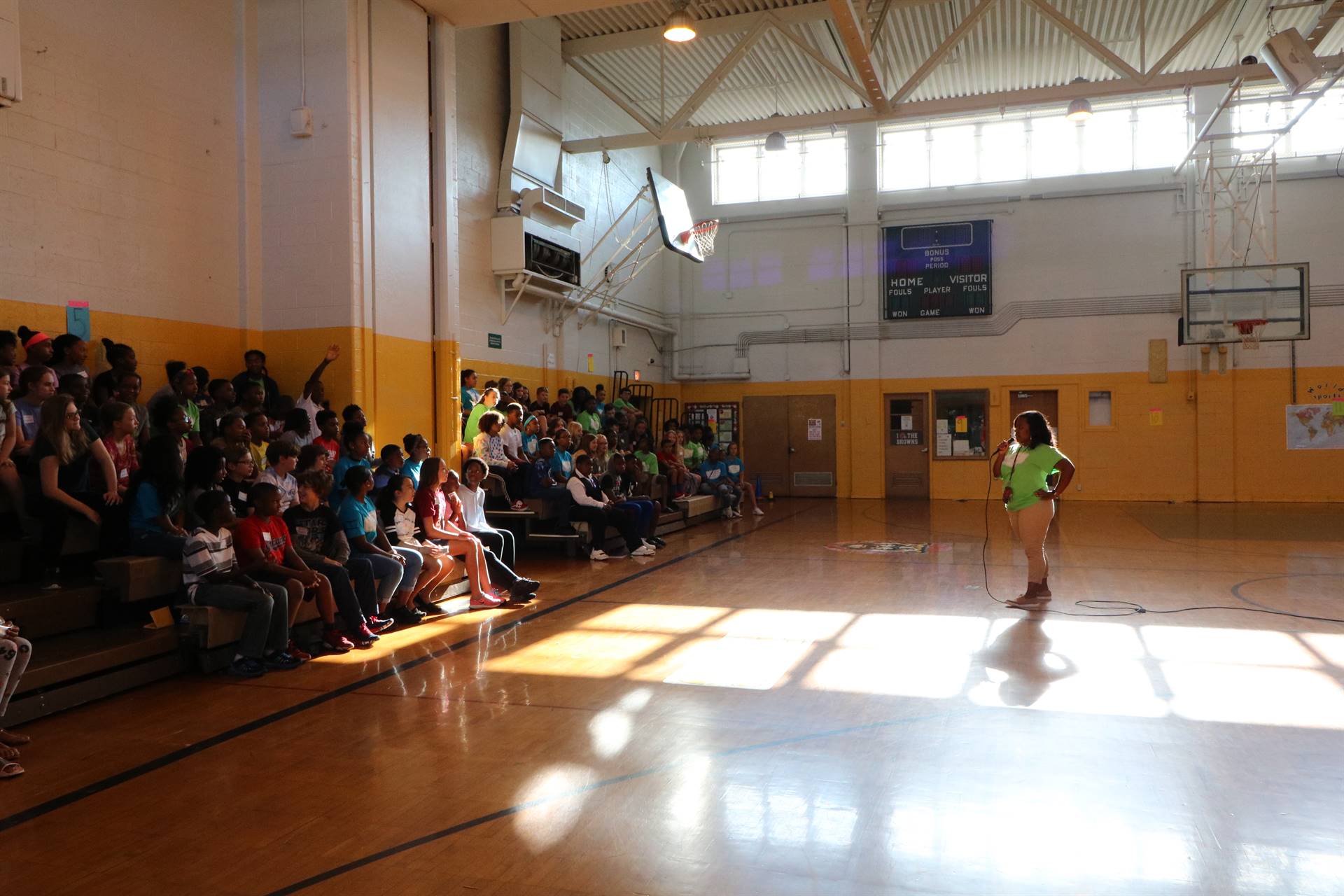 Students sitting in gym bleacher watching teacher speak